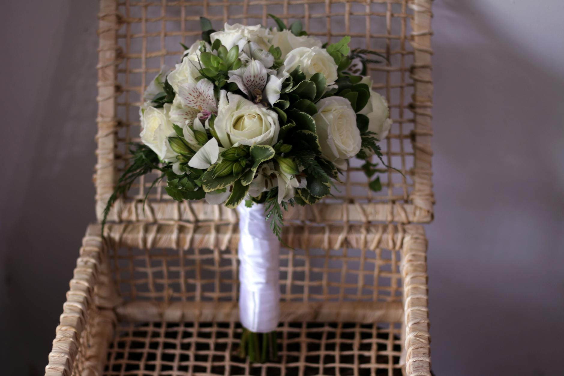 Bukiet białych róż z zielenią na wiklinowym krześle jako dekoracja ślubna