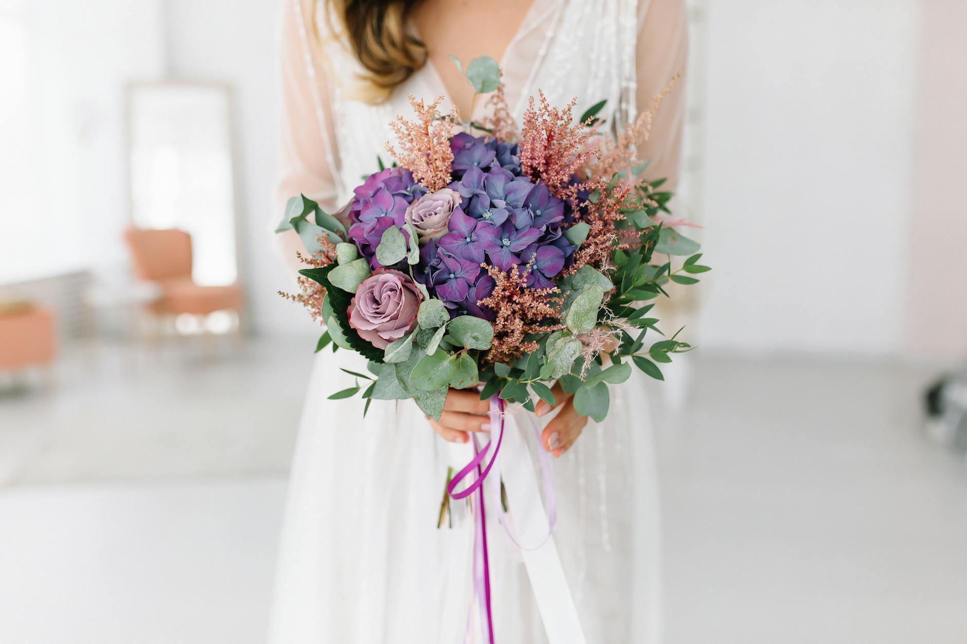 Panna młoda trzyma pastelowy bukiet z fioletowymi hortensjami i różami
