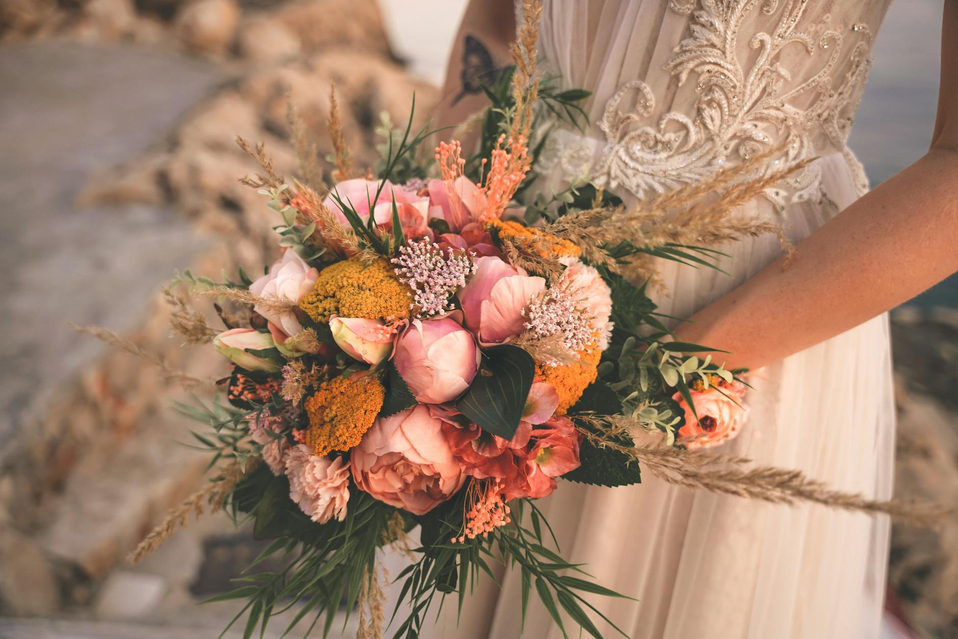 Panna młoda trzyma romantyczny bukiet ślubny w różowo-pomarańczowych barwach