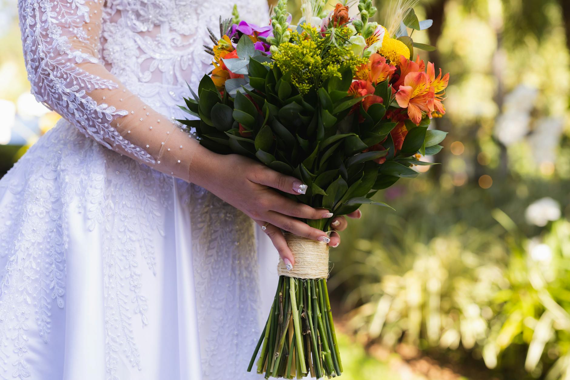 Panna młoda w koronkowej sukni trzyma kolorowy bukiet na świeżym powietrzu