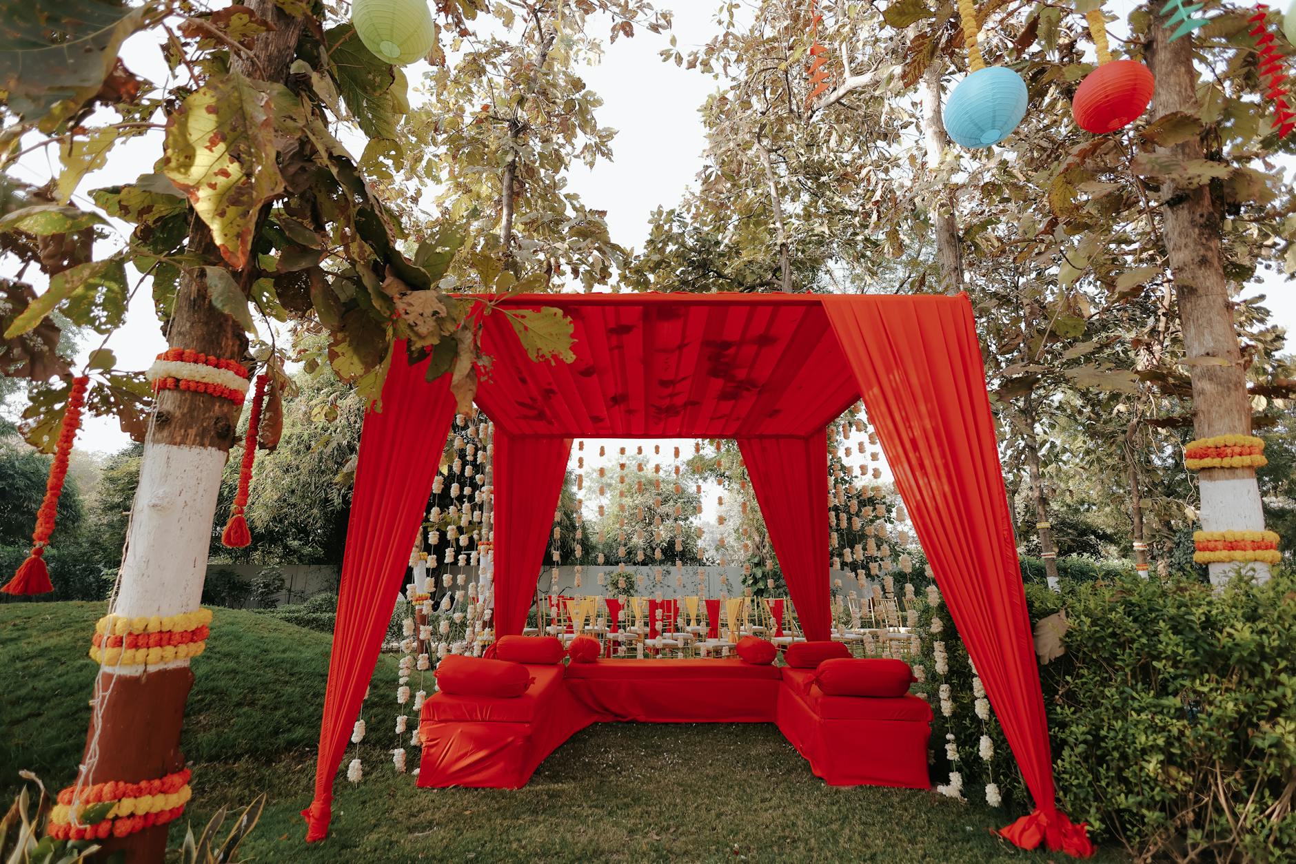 Plenerowa dekoracja ślubna z czerwonym zadaszeniem, lampionami i kwiatami