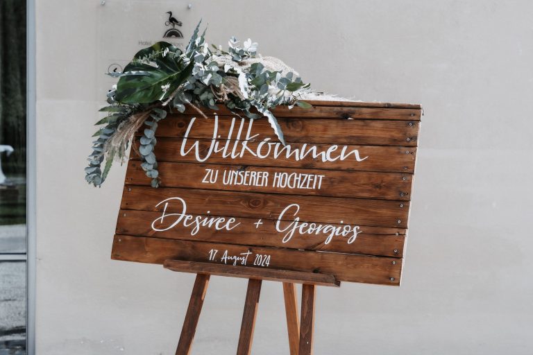 Tablica powitalna przed wejściem na ceremonię: teksty, sztalugi i kompozycje florystyczne